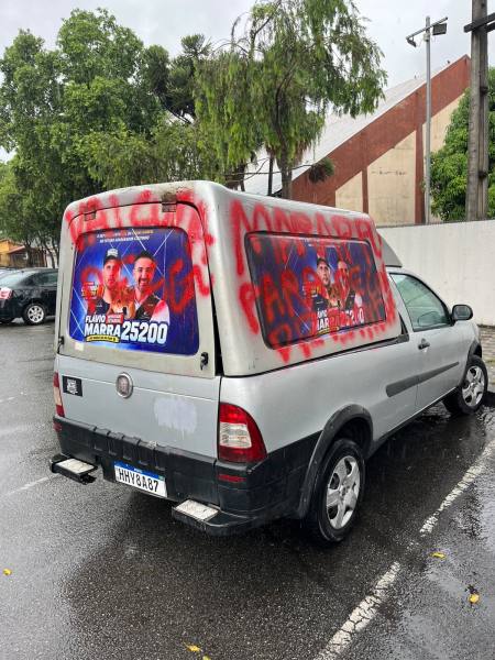 Veículo fechado com propaganda eleitoral na traseira, exibindo os rostos de candidatos e a numeração 25200, com pichações vermelhas visíveis.