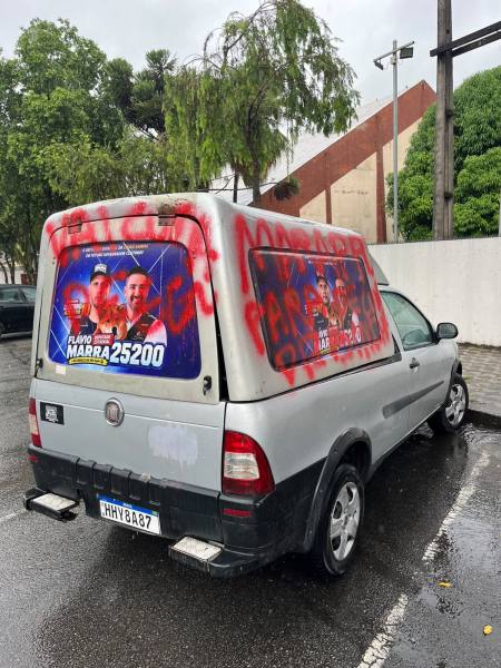 Veículo de carga com propaganda política na parte traseira, coberto com grafite e estacionado em uma rua molhada.
