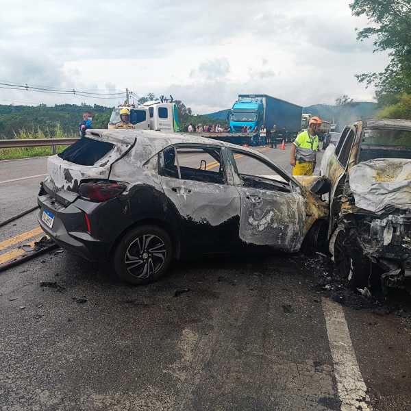 Carro queimado após acidente em estrada, com socorristas trabalhando na cena.