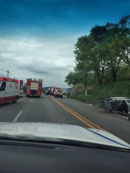 Acidente de trânsito com veículos danificados na estrada, com ambulâncias e bombeiros presentes no local.