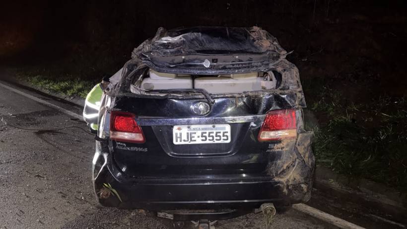 Um carro preto com o teto danificado e sujo, estacionado em uma estrada à noite.