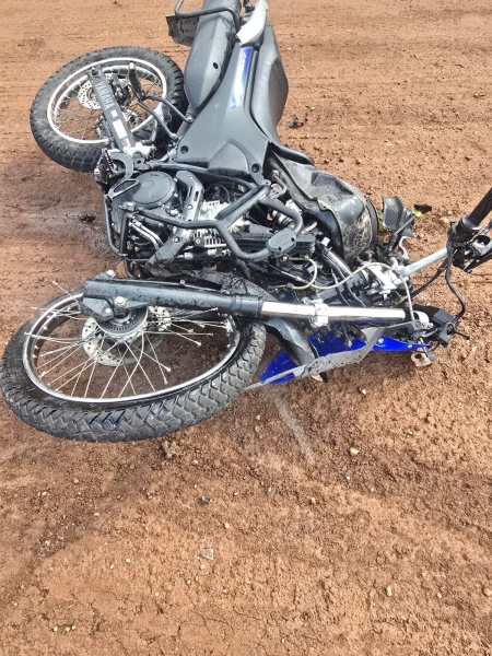 Motocicleta caída em um terreno de terra, com sua roda traseira voltada para cima.