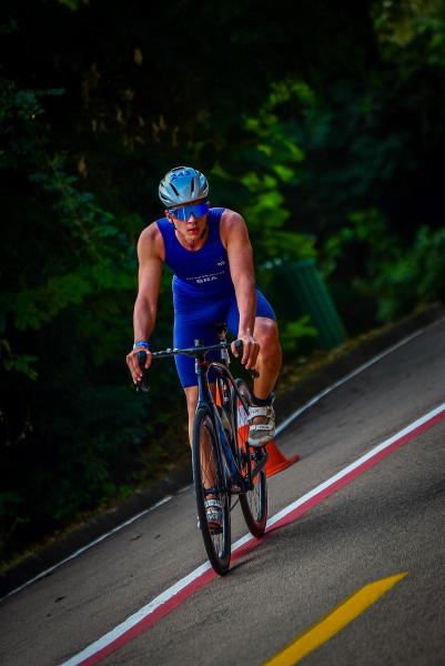 Atleta em uma bicicleta pedalando em uma estrada rodeada por árvores.