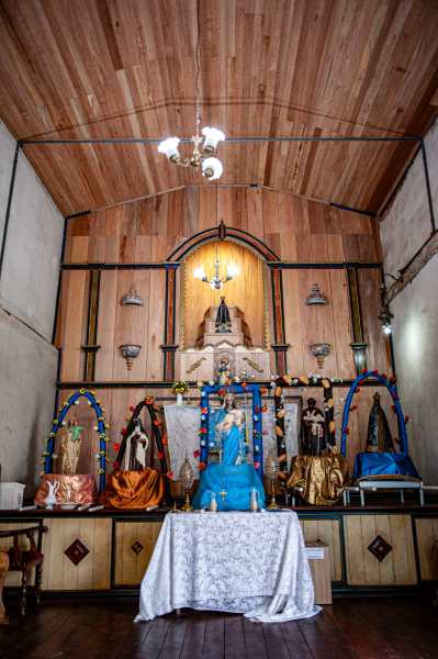 Altar com várias estátuas de santos e uma imagem de Nossa Senhora, decorado com tecido azul e elementos coloridos em um ambiente interno.