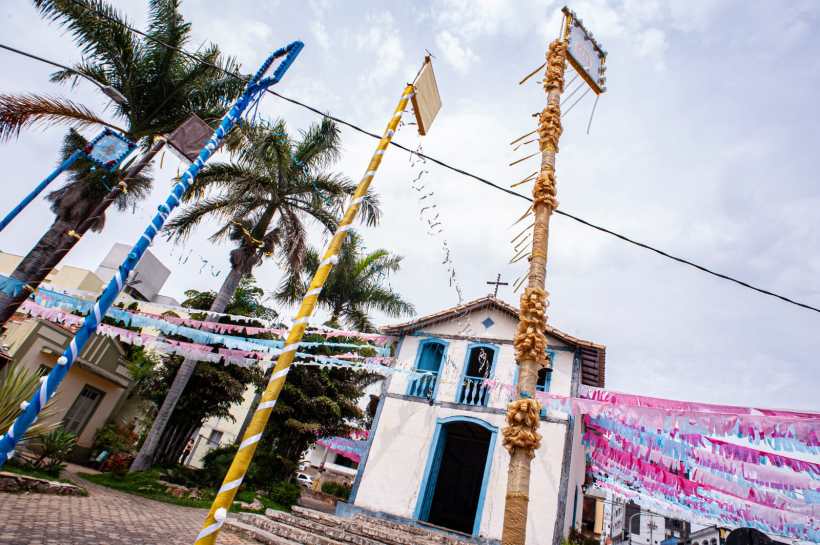 Igreja decorada com bandeirinhas coloridas e palmeiras ao redor, com postes adornados na frente.