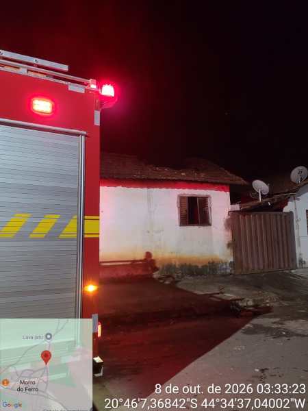 Foto noturna de um caminhão de bombeiros com luzes vermelhas, próximo a uma casa com paredes brancas e janelas escuras, e uma antena parabólica visível. Um mapa do Google no canto inferior esquerdo mostra a localização.