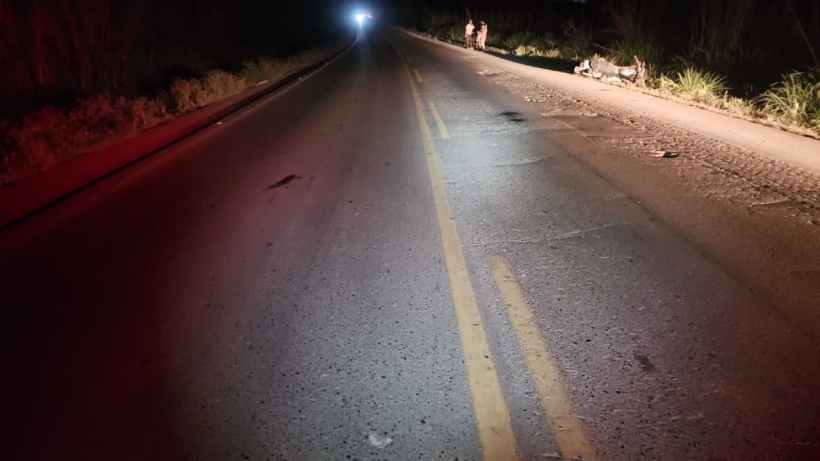 Estrada deserta à noite, com luz ao fundo e faixa de pedestres visível.