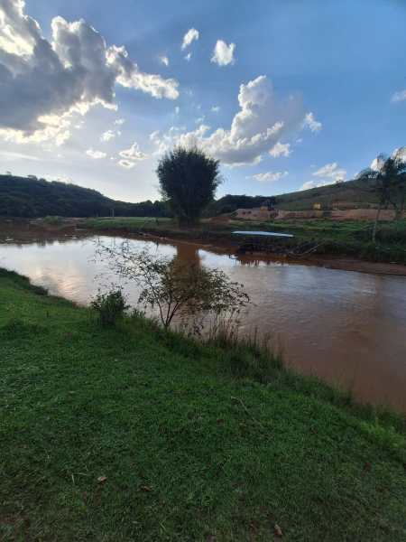 Paisagem tranquila com um rio alagado refletindo o céu, cercado por árvores e montanhas ao fundo.