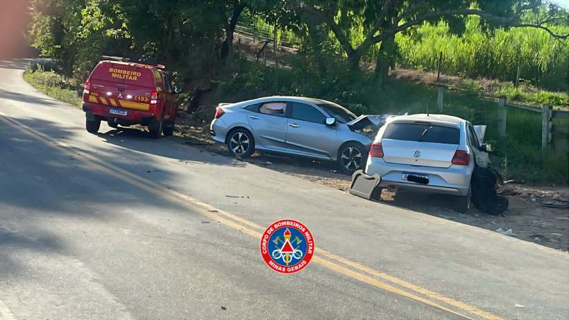 Imagem de um acidente de carro na estrada, com dois veículos danificados: um carro prata e um carro branco. Um veículo de bombeiros está presente na cena.
