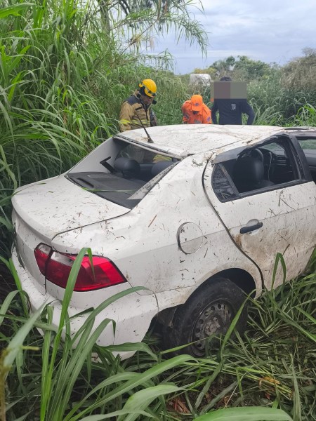 Veículo acidentado em meio a alta vegetação, com equipes de resgate avaliando a situação.