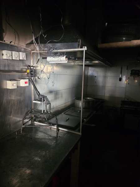 Cozinha escura com um balcão de metal, equipamentos de cozinha e fiação exposta.