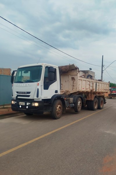 Caminhão basculante da marca Iveco estacionado em uma rua, com caçamba carregada de materiais.