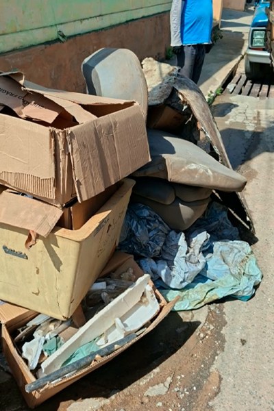 Montagem de lixo, incluindo caixas de papelão e móveis descartados, em uma calçada.