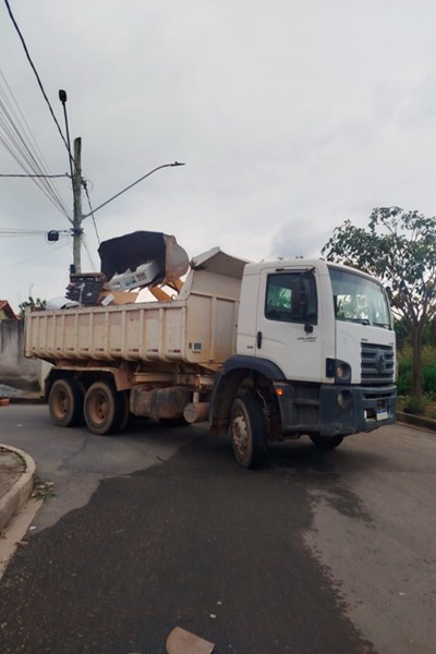 Caminhão de lixo manobrando em uma esquina com entulho na caçamba.