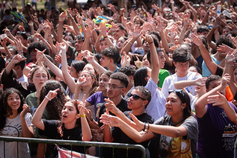 Multidão animada de jovens com as mãos levantadas durante um evento ao ar livre.