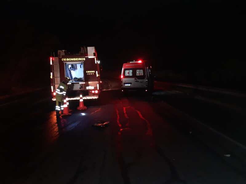Veículo dos bombeiros e ambulância em uma estrada à noite, com um bombeiro trabalhando em frente ao caminhão.
