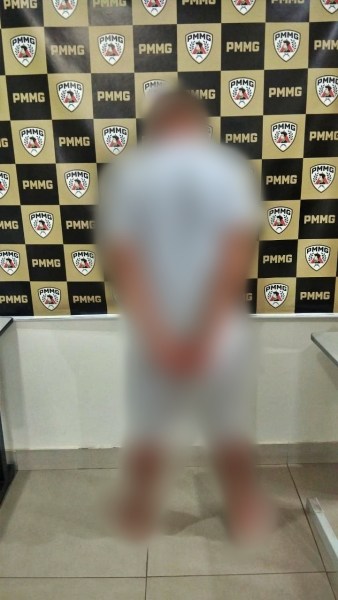 Pessoa de costas em um ambiente policial, com uma parede decorada com emblemas da PMMG ao fundo.
