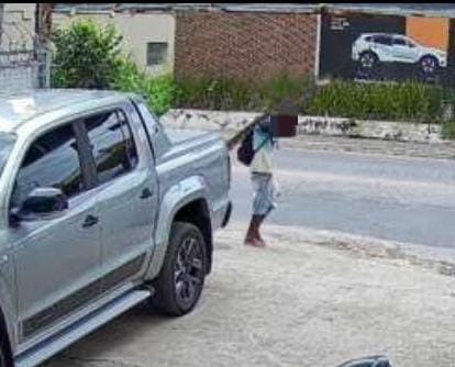 Pessoa caminhando na calçada, próxima a um carro prateado e uma rua tranquila.