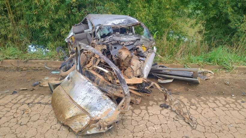 Veículo danificado em um acidente, com a carroceria amassada e partes expostas, situado em uma estrada de terra.