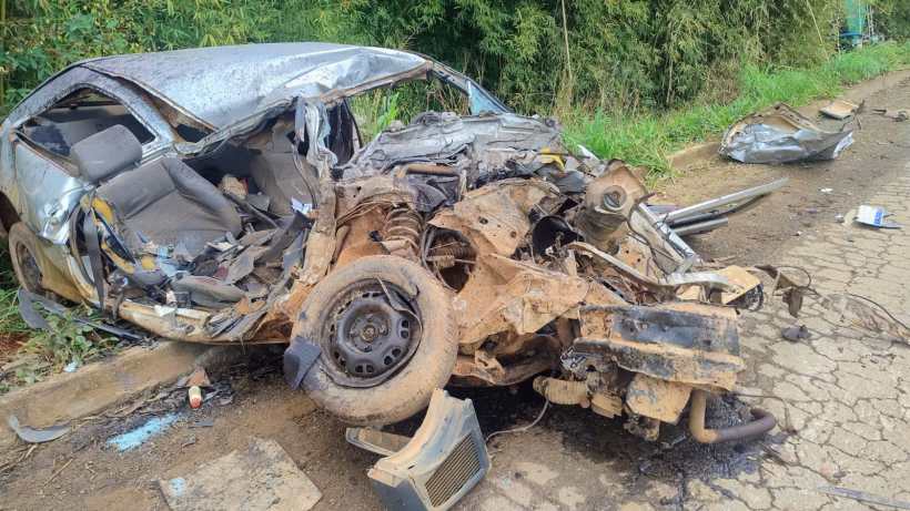 Um carro gravemente danificado após um acidente, com a carroceria em colapso e os assentos expostos, localizado ao lado de uma estrada.
