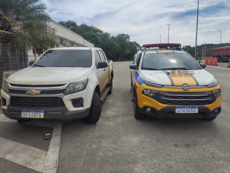 Uma caminhonete Chevrolet suja estacionada ao lado de um veículo de patrulha Fiat com pintura azul e amarelo.