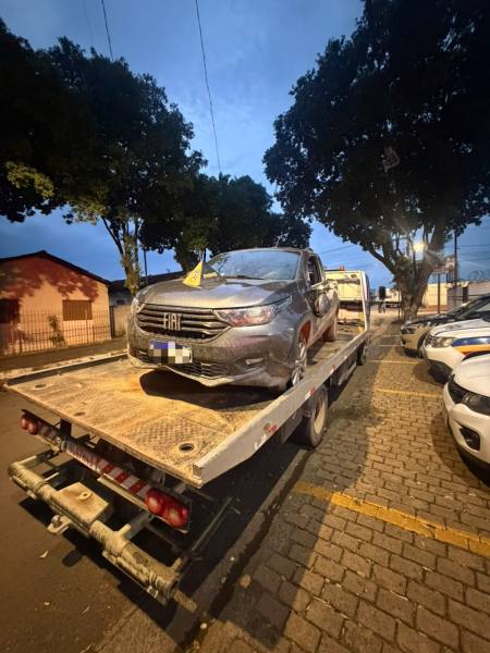 Um carro Fiat em uma plataforma de reboque estacionada em uma rua arborizada durante o anoitecer.