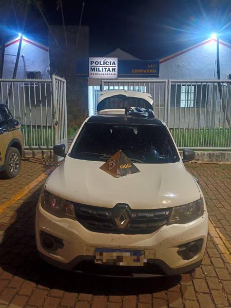 Veículo da Polícia Militar estacionado em frente à unidade policial à noite, com placa de identificação sobre o capô.