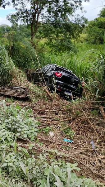Um carro preto capotado entre a vegetação e os arbustos.