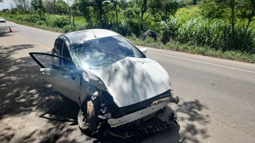 Carro acidentado na beira da estrada, com parte dianteira danificada e porta aberta.