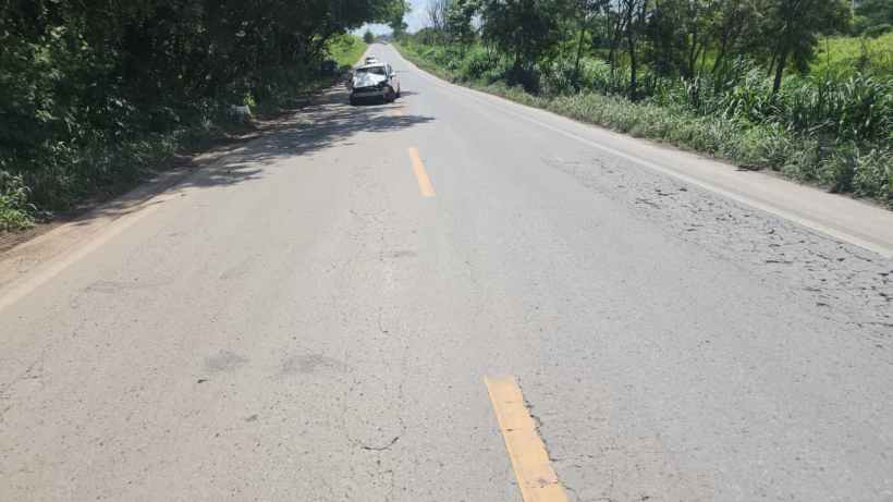 Vista de uma estrada pavimentada com faixas amarelas, vegetação à beira da estrada e um carro estacionado ao lado.