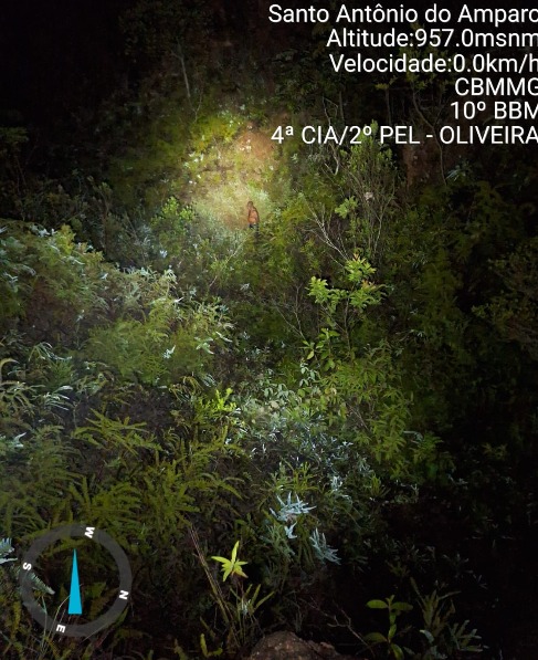 Cena noturna de vegetação densa com um foco de luz iluminando o caminho em Santo Antônio do Amparo. Informações de altitude e localização no canto superior direito.