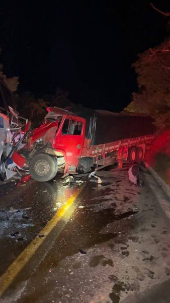 Caminhão vermelho danificado em um acidente à noite na estrada, com detritos espalhados pela pista.