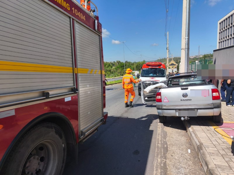 Veículo acidentado na via, com equipe de resgate e caminhão de bombeiros ao fundo.