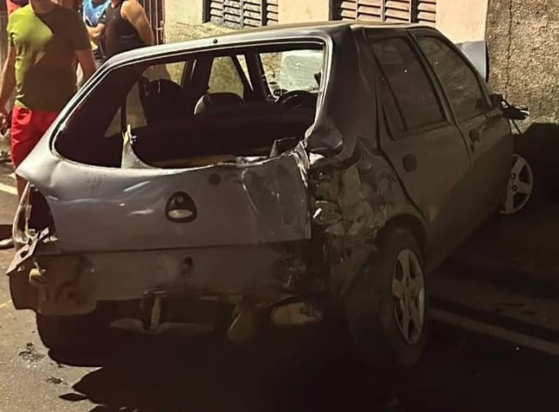 Um carro acidentado estacionado na calçada, mostrando danos significativos na traseira, em um ambiente noturno.