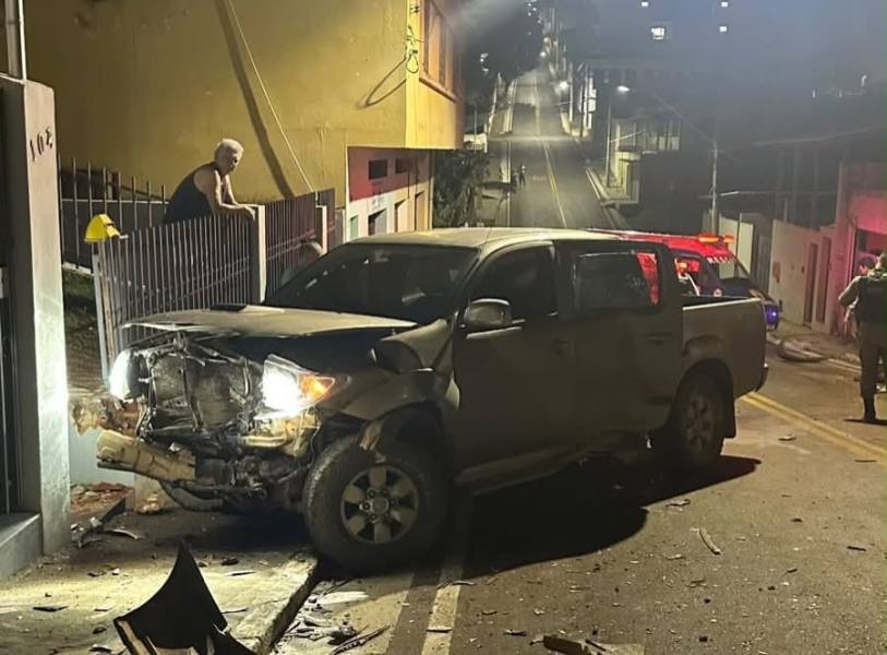 Um caminhão danificado após um acidente de carro, com um homem observando de perto e uma rua iluminada ao fundo.