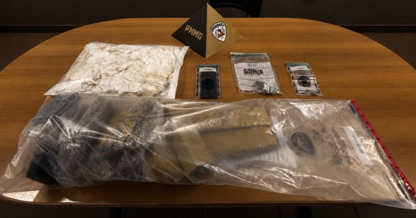 Material apreendido em uma mesa, incluindo drogas em bolsas plásticas, documentos e um triângulo com a marca da PMMG.