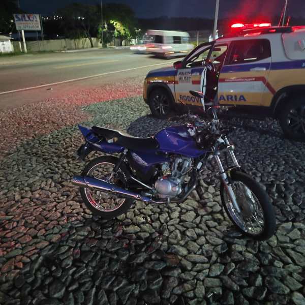 Uma moto azul estacionada em frente a um veículo da polícia rodoviária, em um ambiente noturno.
