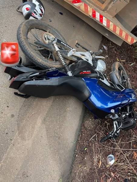 Motocicleta azul caída ao lado da estrada, com um capacete branco e um sinal luminoso vermelho ao fundo.