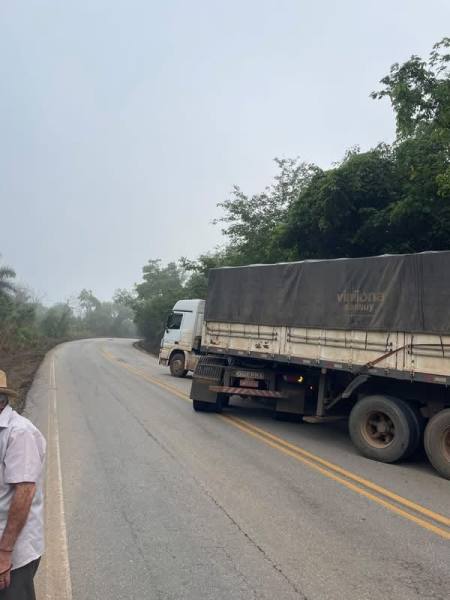 Caminhão estacionado em uma estrada sinuosa, cercado por vegetação densa e neblina.
