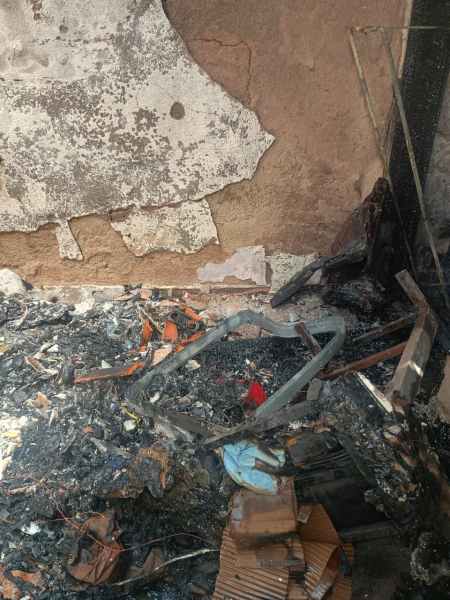 Ambiente devastado por incêndio, com restos de materiais queimados e paredes danificadas.