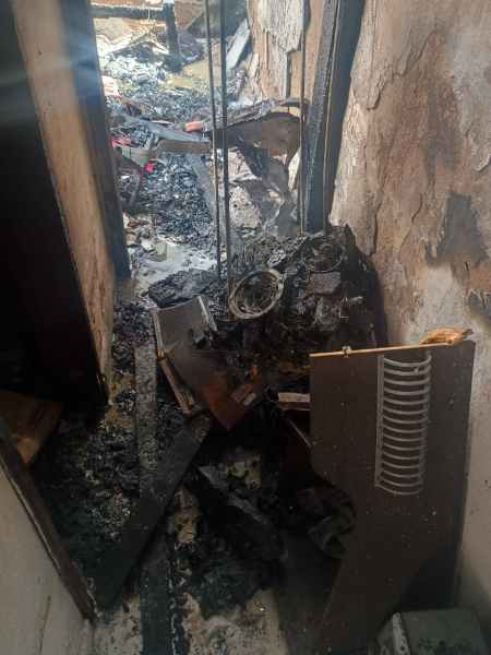 Corredor danificado por incêndio, com paredes queimadas e escombros pretos no chão.