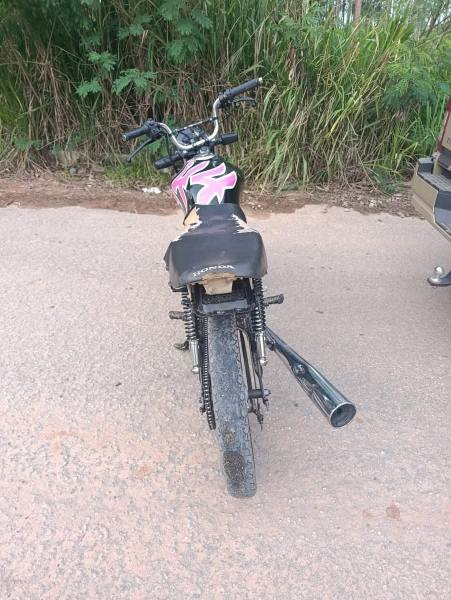 Vista traseira de uma bicicleta com selim danificado, guidão preto e detalhes em rosa, estacionada em uma estrada com vegetação ao fundo.