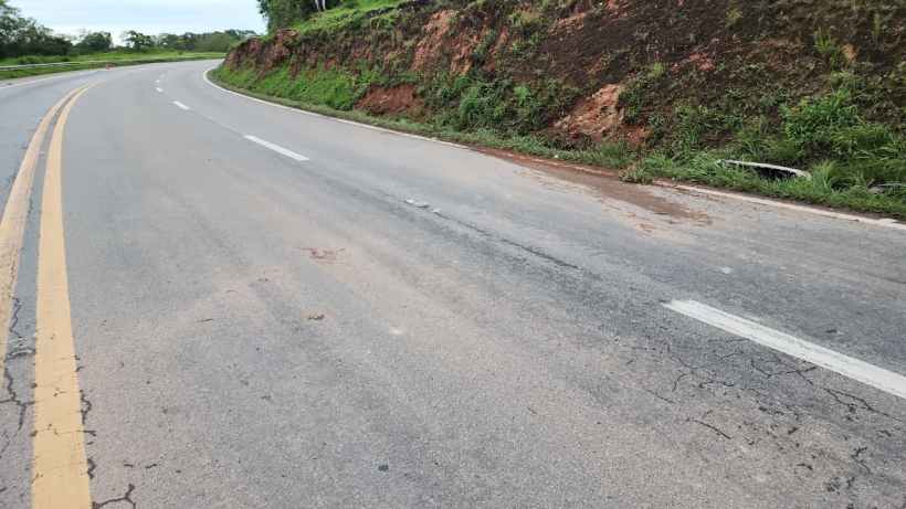 Trecho de estrada curvado, com marcas de desgaste no asfalto e vegetação ao lado.