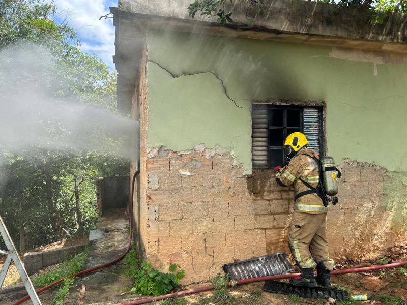 Um bombeiro utilizando equipamentos de proteção combate um incêndio em uma casa, enquanto jatos de água são direcionados para uma janela.