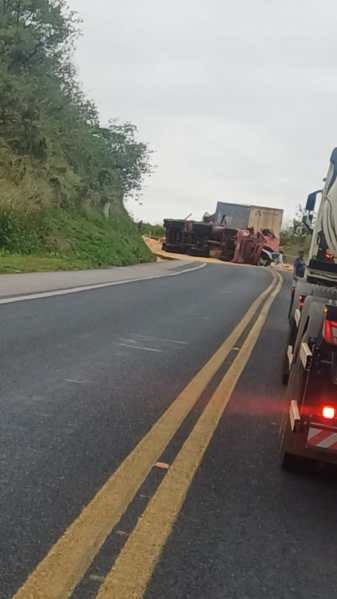 Caminhão tombado em uma estrada com vegetação ao redor.