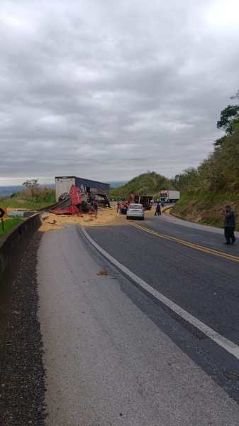 Acidente de caminhão na estrada, com carga derramada e veículos parados ao lado da via.