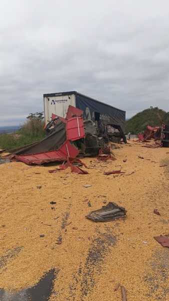 Caminhão tombado na estrada, com carga de milho espalhada pelo chão e destroços ao redor.