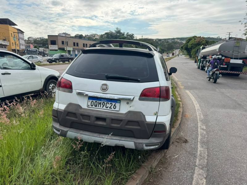 Um carro branco estacionado na beira da estrada, ligeiramente encostado na grama.