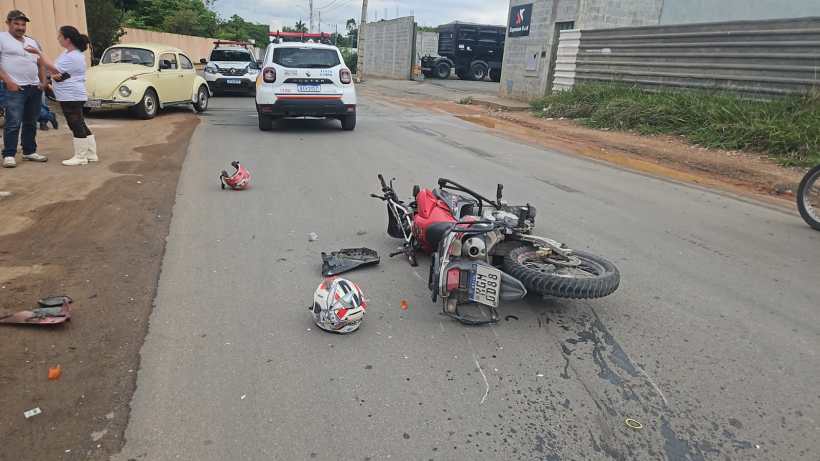 Moto caída na estrada com capacete ao lado, cenário de acidente. Pessoas observando, veículos de polícia presentes.