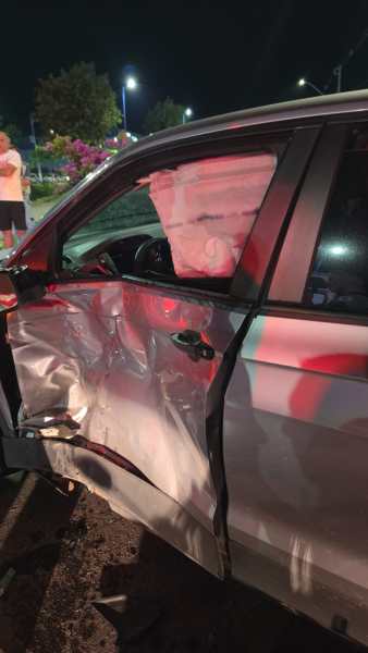 Carro danificado com porta amassada após acidente, visível em iluminação noturna.